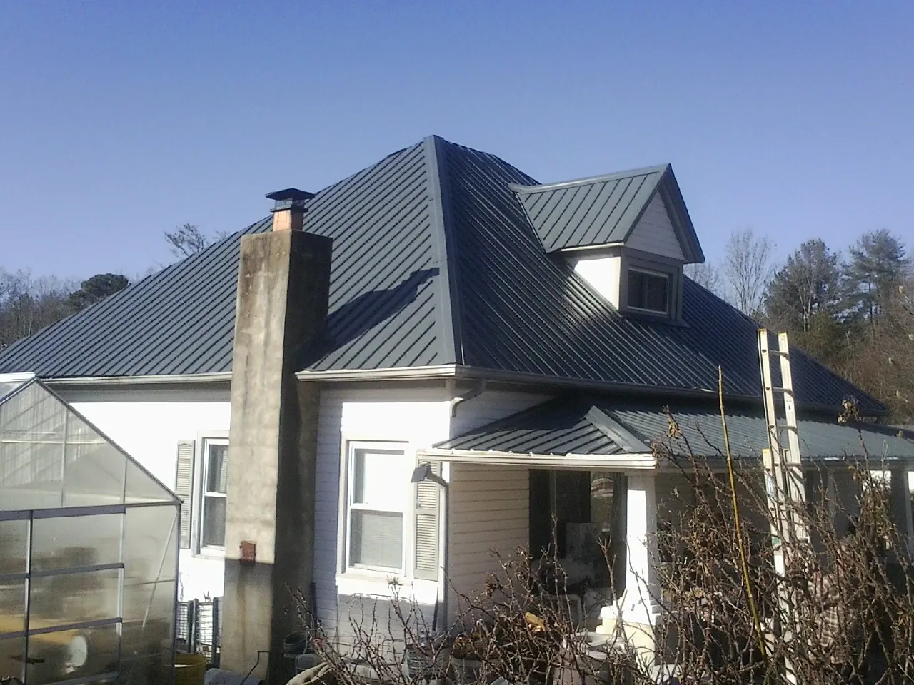 Dark blue standing seam metal roof on a white farmhouse with dormer — Slate & Tile Roof Repair by Roofing Brothers in Issue