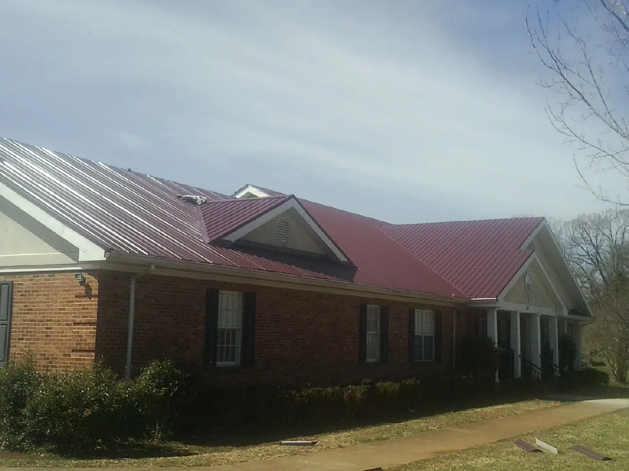 Red metal roof with gabled entries on a long brick building, from a Hail Damage Roof Repair job in Issue