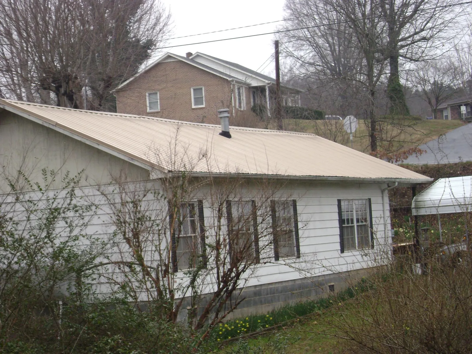Tan metal roof on a white sided house set into a hillside — Commercial Roofing by Roofing Brothers in Issue